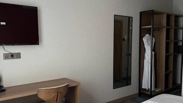 A hotel room with a desk, chair, two beds, a TV, a wardrobe, and a mirror.