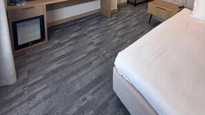 Quarto de hotel com cama, escrivaninha com televisão de tela plana, guarda-roupa e um pequeno espaço de estar.