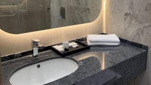 A bathroom with a marble vanity, a sink, a mirror, and a shower area.