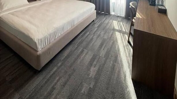 Quarto de hotel com uma cama grande, uma escrivaninha, uma cadeira, uma televisão e uma janela com cortinas.