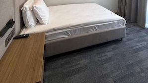 A single bed with a headboard, a bedside table, and a remote control on it.