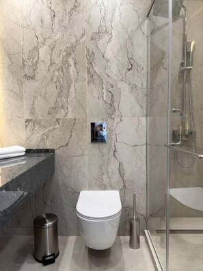 Un baño con pared de mármol, un inodoro, un bote de basura y zona de ducha.