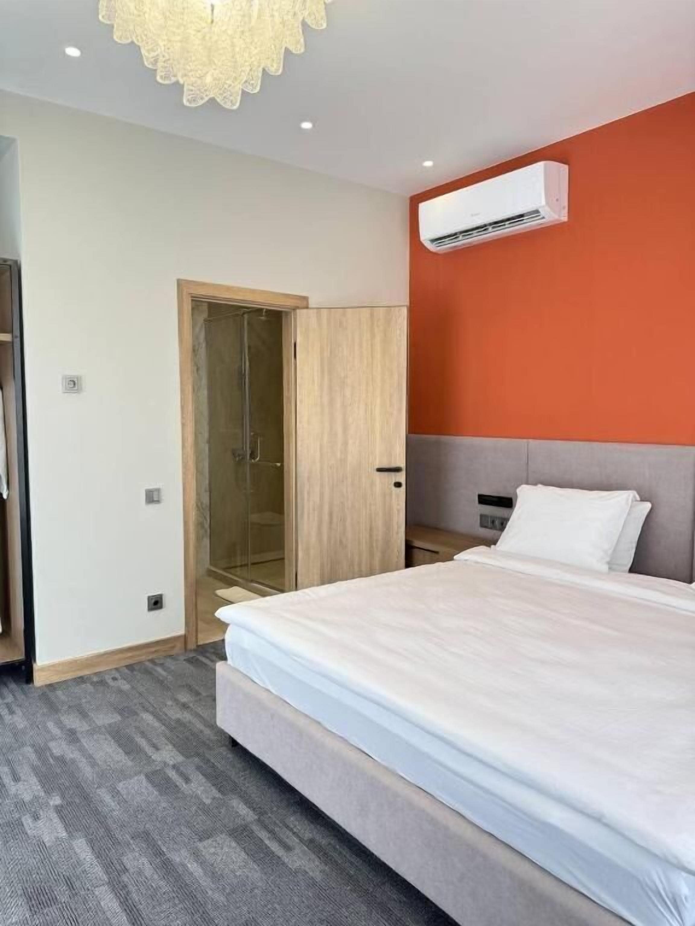 A hotel room with a bed, an air conditioning unit, a wooden wardrobe, and a glass shower enclosure.