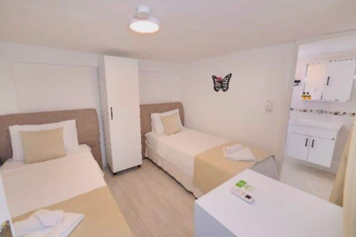 A hotel room with two beds, a desk, a wardrobe, and a butterfly wall decoration.