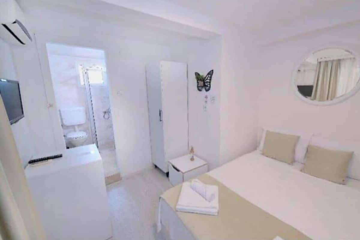 A hotel room with a bed, a bedside table, a mirror, and a door leading to a bathroom.