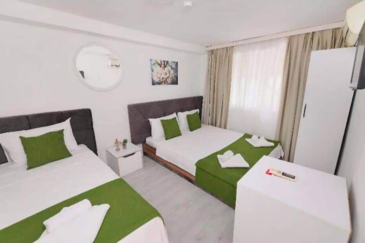 A hotel room with two beds, a round mirror, a small table, and a wardrobe.