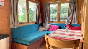Een interieur van een blokhut met een blauwe bank, een houten eettafel en gordijnen voor de ramen.