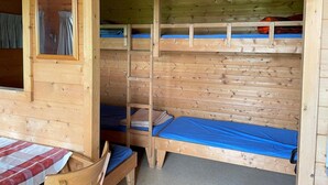 Een houten hut met stapelbedden, een raam met gordijnen en een tafel met een geruit tafelkleed.