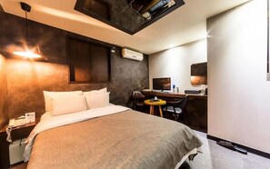 Een hotelkamer met een bed, nachtkastje, bureau, stoel en een klein rond tafeltje.