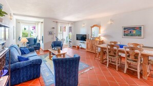 A spacious living area with a sofa, chairs, a dining table, and a TV. - Townhouse Praia da Galé casa 16 (Albufeira)