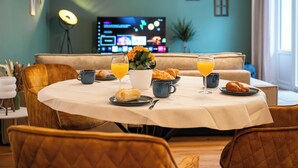 Un comedor con una mesa dispuesta para el desayuno, que incluye cruasanes, jugo de naranja y un florero con flores.