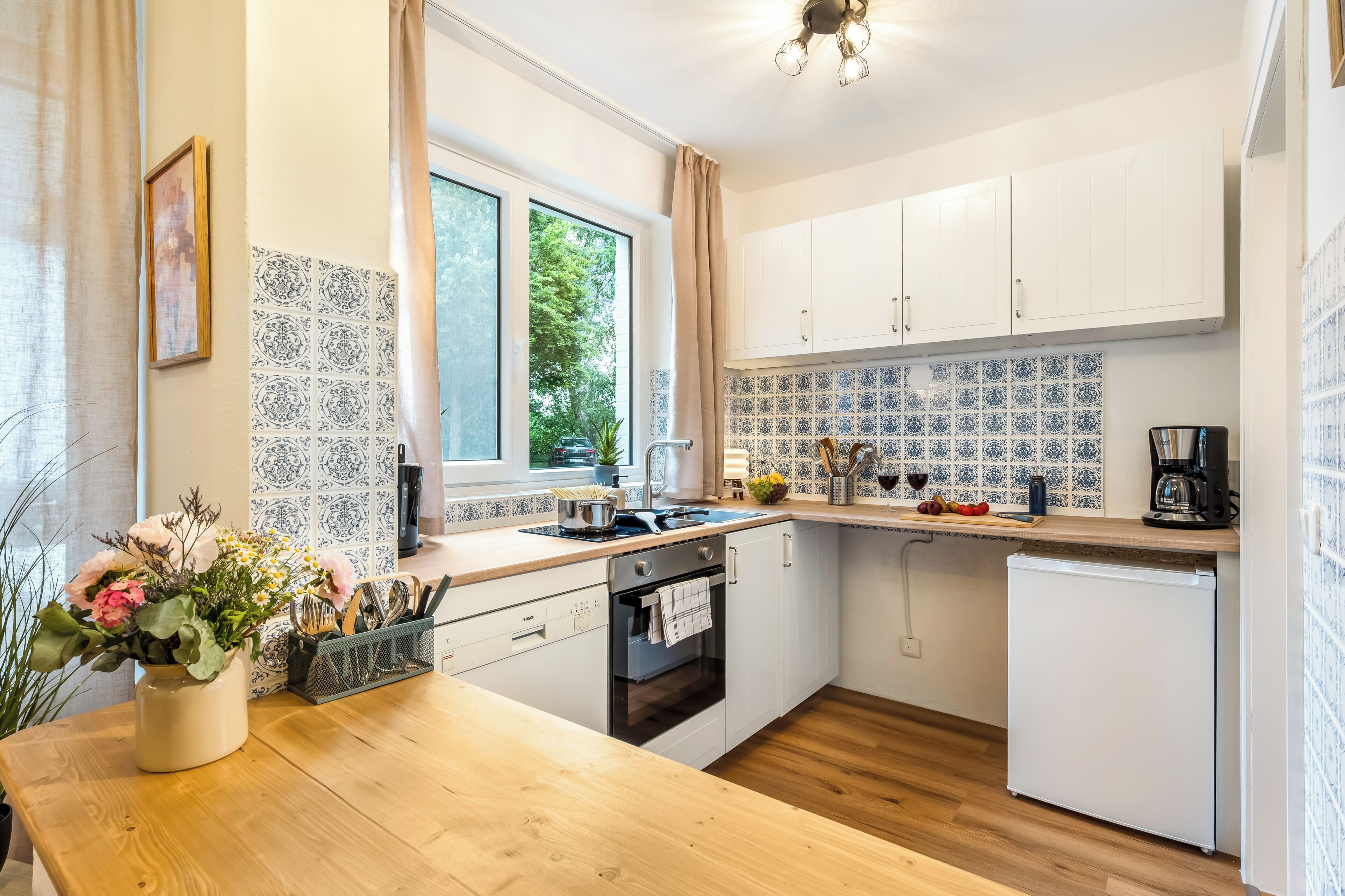 Eine moderne Küche mit weißen Schränken, einer Holz Arbeitsplatte, einer Spüle, einem Herd und einem Kühlschrank.