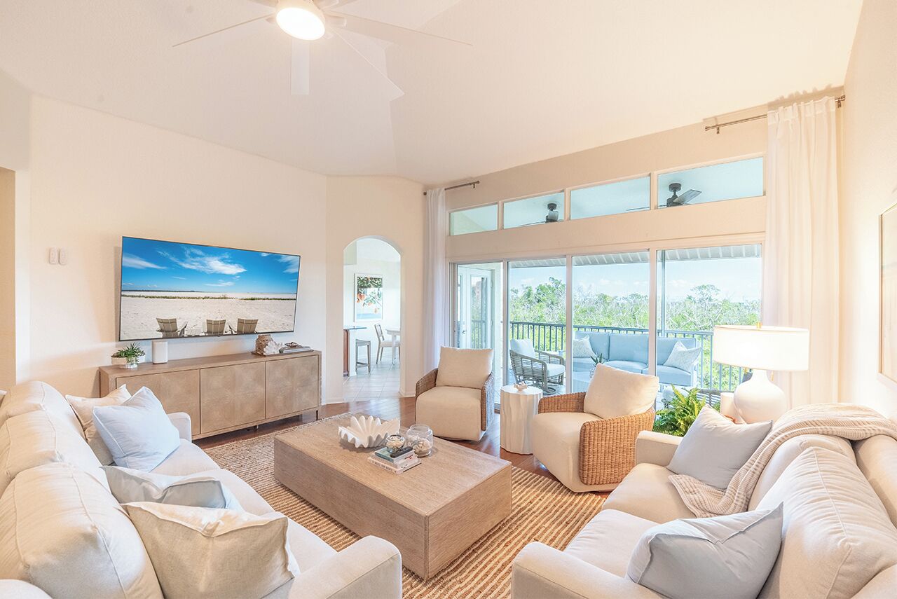 A spacious living room with a large TV, comfortable seating, a coffee table, and a balcony with a view.