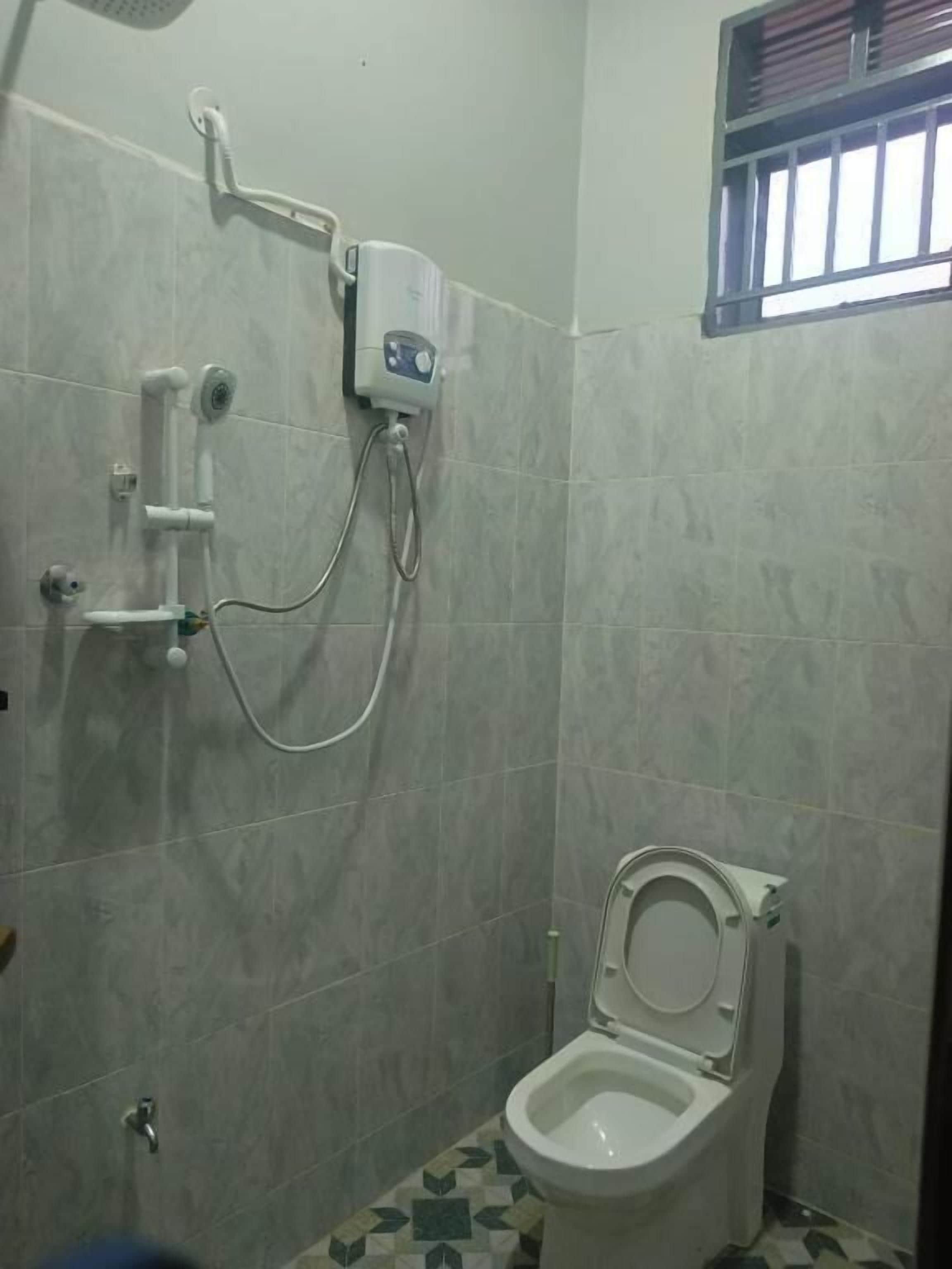 A small bathroom with a toilet, a shower unit, and a window with bars.
