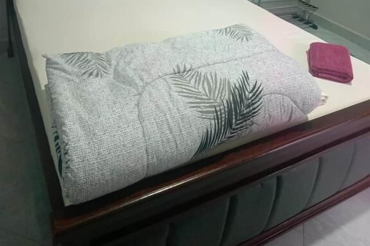 Een bed met een houten hoofdbord, kussens, een deken en een metalen rek.