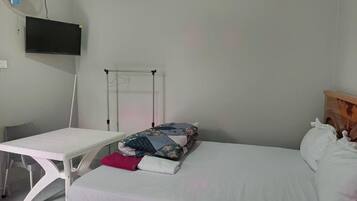 Ein Schlafzimmer mit Bett, Schreibtisch, Stuhl, Wandfernseher und Heizkörper.