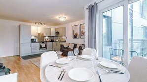 Une cuisine moderne avec des meubles blancs, un coin repas doté d’une table ronde pour quatre personnes et un balcon aménagé avec du mobilier d’extérieur.