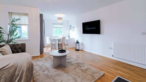 Un salon moderne comprenant un canapé, une table à manger avec des chaises, un téléviseur fixé au mur et un radiateur.