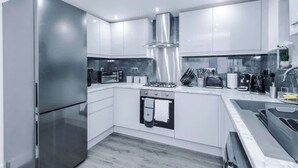 A modern kitchen with stainless steel appliances, white cabinetry, and a marble countertop. - 3BR Elegant House in Leeds | Sleeps 6 | Driveway (West Yorkshire)