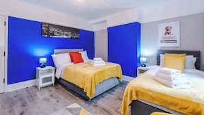 Ett hotellrum med två sängar, var och en med ett gult överkast, vita kuddar och en röd prydnadskudde. Det finns sängbord med lampor, en inramad tavla på väggen och en affisch på väggen.