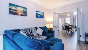 Ett modernt vardagsrum med en blå soffa, en matplats med bord och stolar samt en hall som leder till ett annat rum.