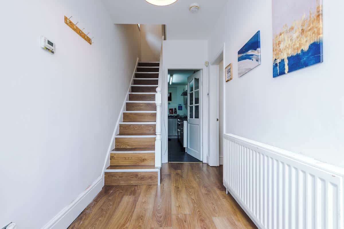 A hallway with a wooden staircase, white walls, and a radiator.