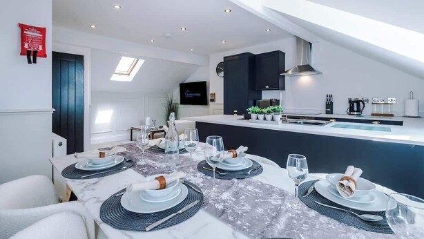 Een moderne keuken met een centraal eiland, verlichting boven en een eethoek voor zes personen.
