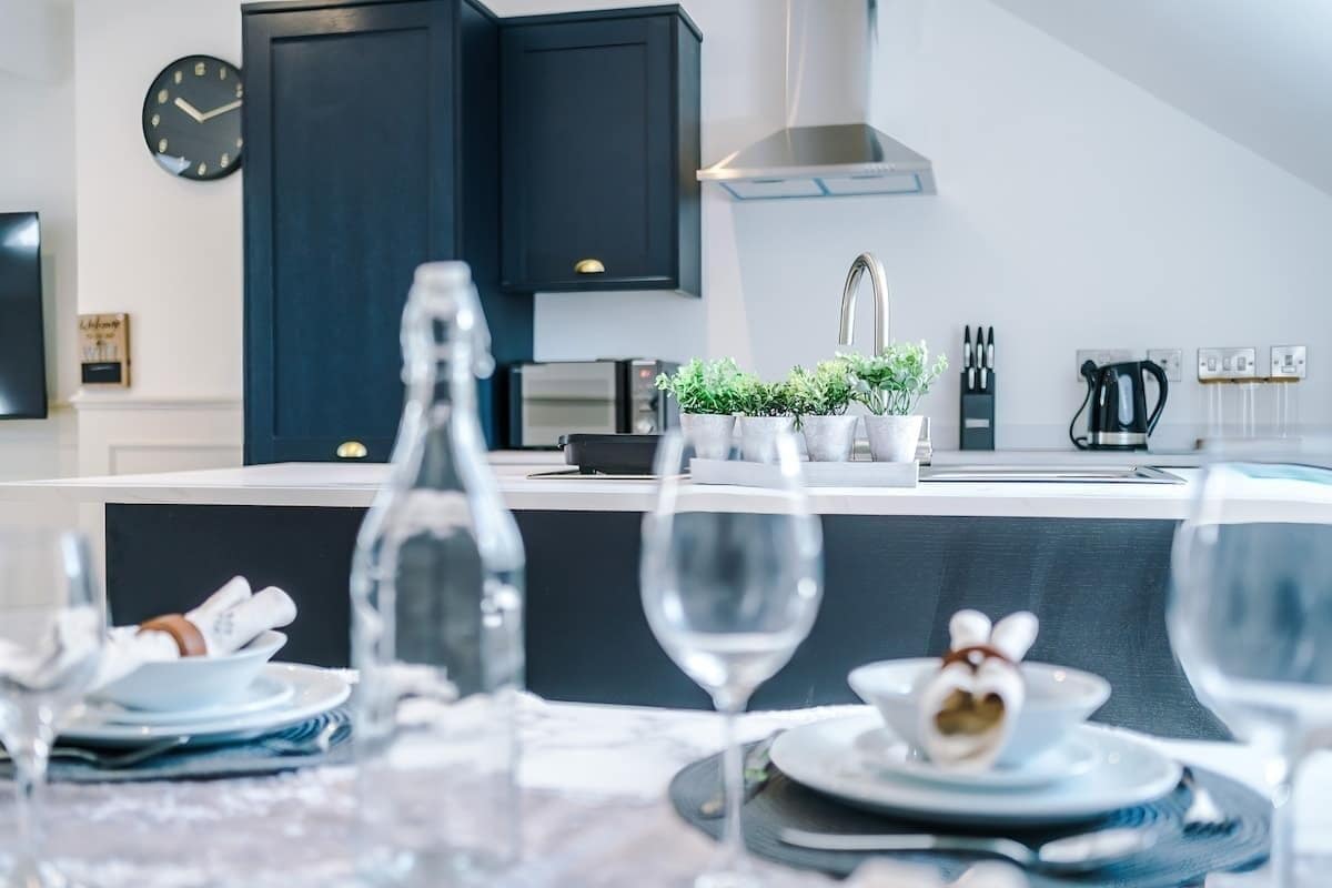 Une cuisine moderne avec des meubles de couleur sombre, un four encastré, une machine à café et une horloge murale.