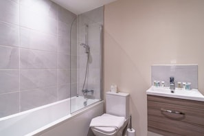 A modern bathroom with a glass-enclosed shower, a white toilet, and a vanity with toiletries. - Spacious Salford Quays Apartment, Prime Location (Greater Manchester)