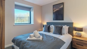 Una camera da letto con un letto, una finestra, un comodino, una lampada e un quadro appeso al muro.