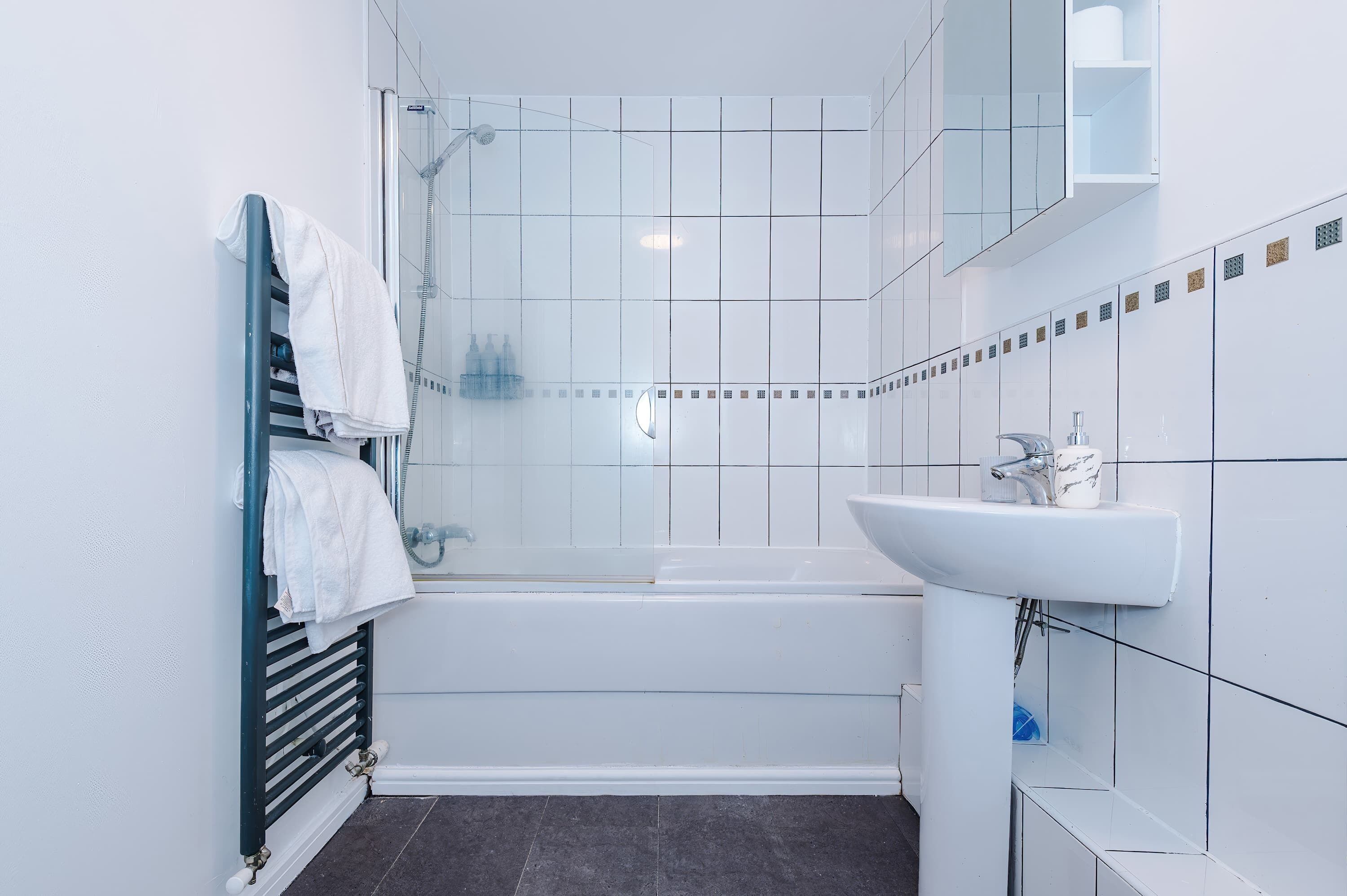 Un baño moderno con ducha de vidrio, lavamanos blanco y un perchero para toallas.