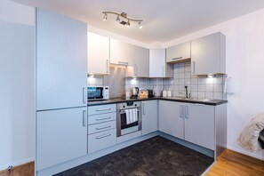 A modern kitchen with white cabinets, a microwave, a kettle, and a sink.