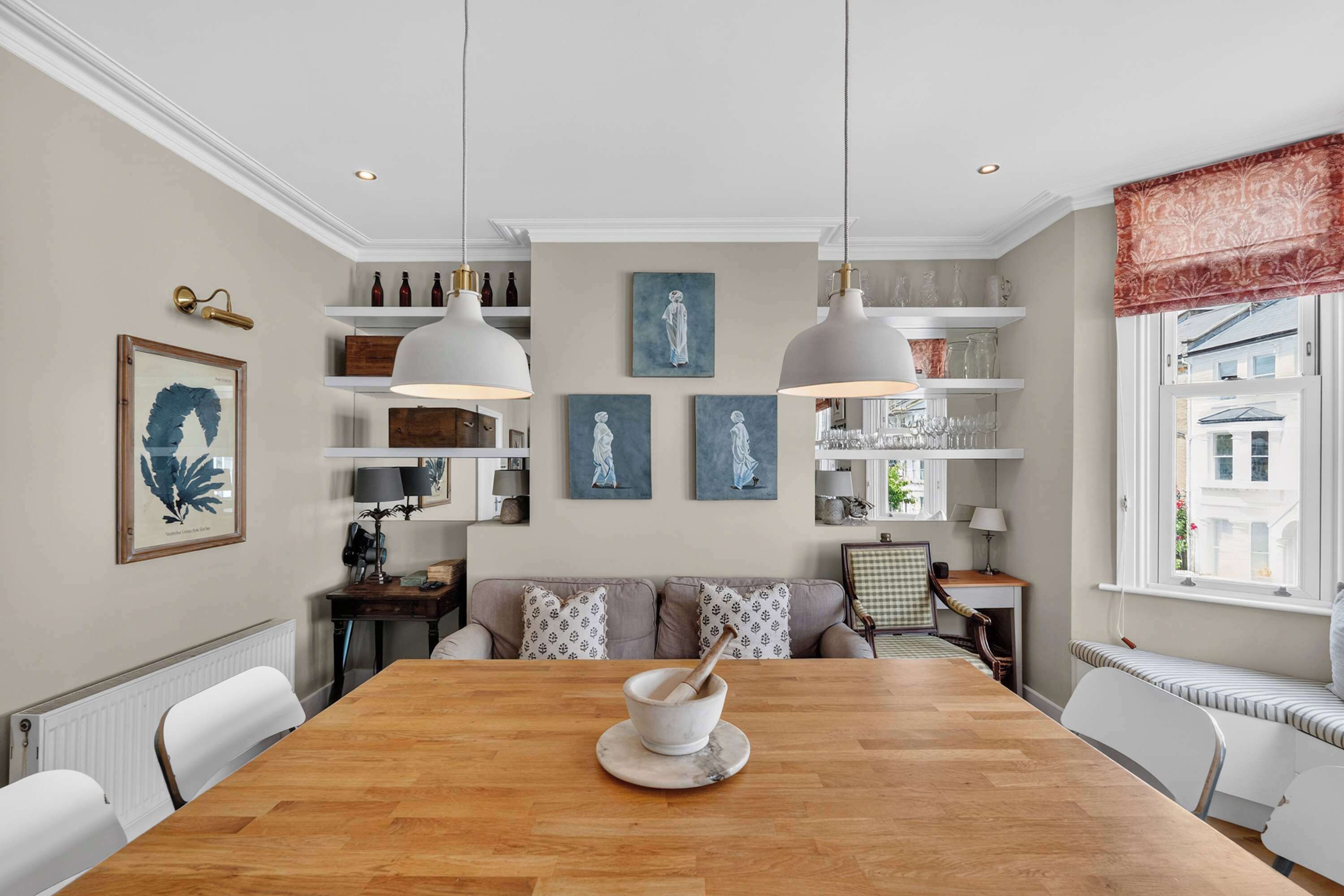 A dining room with a wooden table, white chairs, pendant lights, and artwork on the walls.