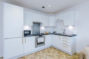A modern kitchen with white cabinets, gold handles, a black countertop, and a herringbone wood floor. - Spacious 2BR | Sleeps 6 | Parking | Walk to Etihad (Greater Manchester)
