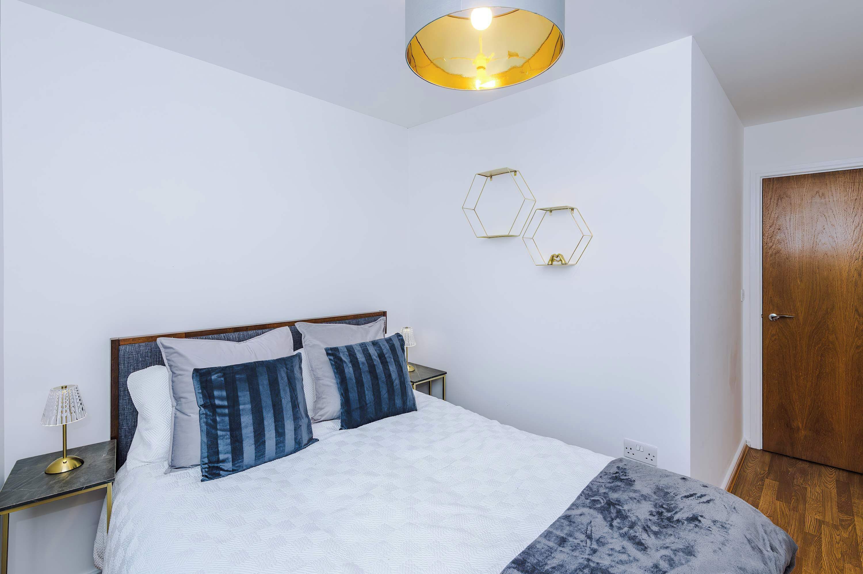 A bedroom with a bed, bedside tables, a lamp, a wooden door, and a wall-mounted light fixture.