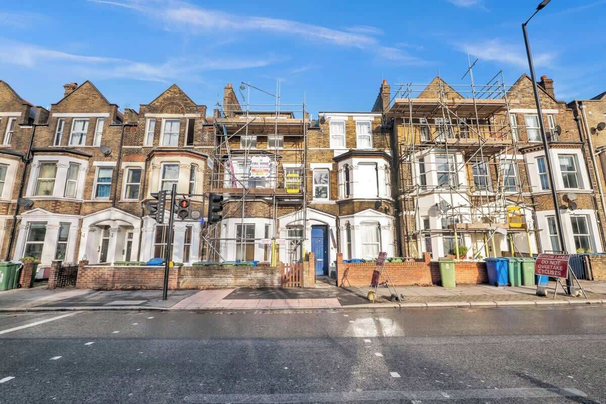 A row of terraced houses under construction with scaffolding, a traffic light, and a 'Do Not Overtake Cyclists' sign.