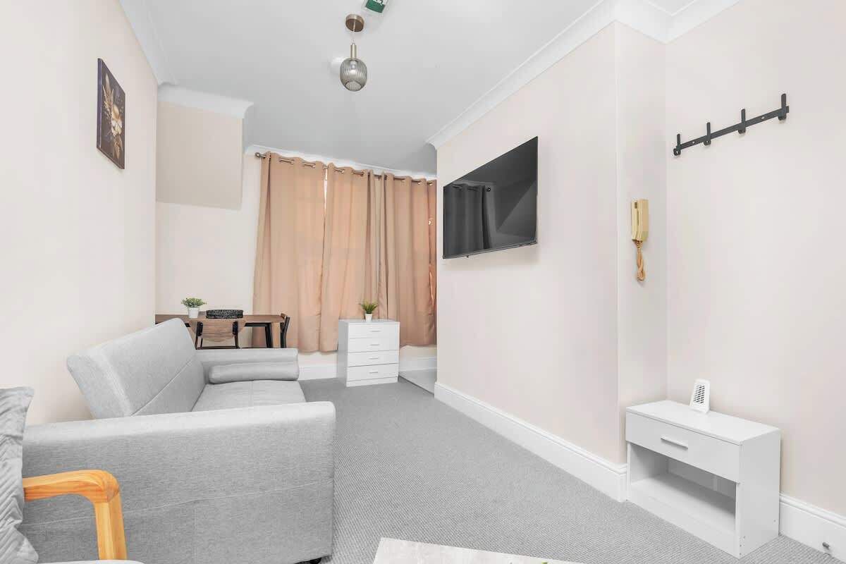 A modern living room with a grey sofa, a small white table, a mounted TV, and a coat rack.