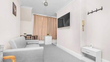 A modern living room with a grey sofa, a small white table, a mounted TV, and a coat rack.