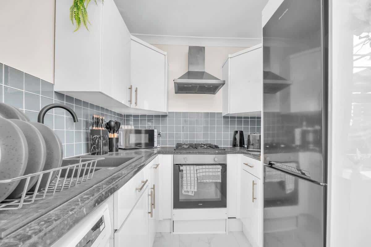A modern kitchen with white cabinets, a stainless steel range hood, a built-in oven, and a microwave.