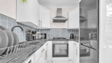 A modern kitchen with white cabinets, a stainless steel range hood, a built-in oven, and a microwave.