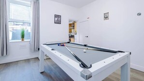 Ein Billardtisch in einem Raum mit Fenster, Tür und Blick auf eine Stadtlandschaft.
