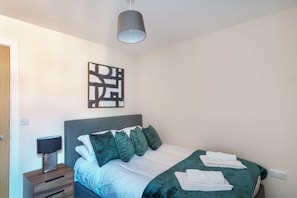 A bedroom with a bed, a bedside table, a lamp, and a wall art piece. - Apartment for 2 | Salford | All Amenities (Greater Manchester)