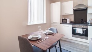 Ett modernt kök med vita skåp, en mikrovågsugn, en ugn och ett matbord med plats för två personer.