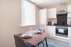 A modern kitchen with white cabinets, a microwave, an oven, and a dining table set for two. - Apartment for 2 | Salford | All Amenities (Greater Manchester)