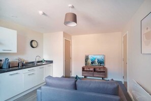 A modern kitchen with white cabinets, a grey sofa, and a painting on the wall. - Apartment for 2 | Salford | All Amenities (Greater Manchester)