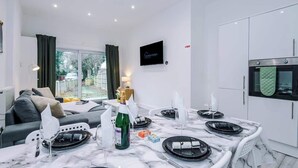 Ein modernes Wohnzimmer mit Essbereich, einem an der Wand montierten Fernseher und einer Küche mit weißen Schränken und Backofen.