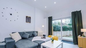 Ein modernes Wohnzimmer mit einem grauen Sofa, einem weißen Couchtisch, einer Uhr und einem Fenster mit Vorhängen.