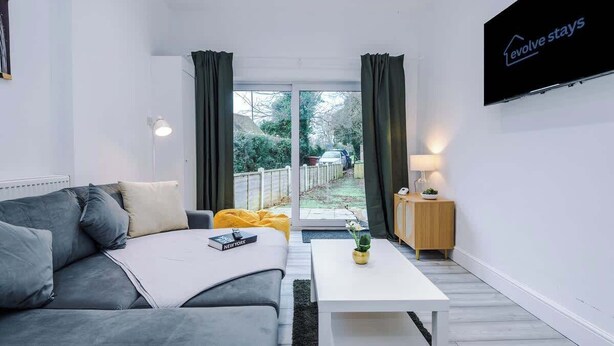 Ein modernes Hotelzimmer mit grauem Sofa, einem weißen Couchtisch, einem an der Wand montierten Fernseher und einer Glastür, die auf einen Balkon führt.