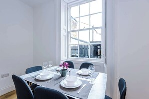 A dining table set for four with white plates, glasses, and a vase of flowers. - Sleeps 6 | 2BR Apartment | Central Otley Location (West Yorkshire)