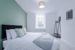 A bedroom with a bed, a window, a standing lamp, and a framed picture on the wall. - Sleeps 6 | 2BR Apartment | Central Otley Location (West Yorkshire)